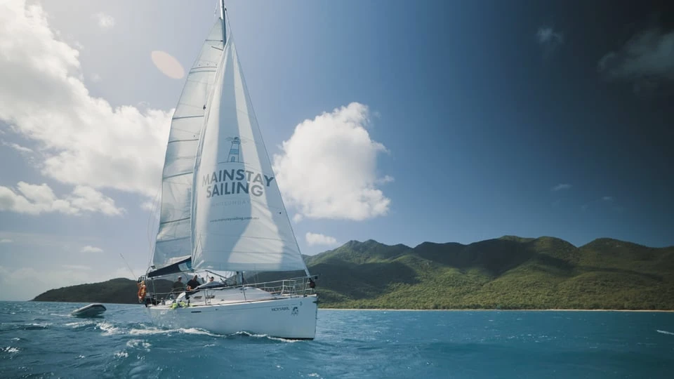 Mainstay Sailing yacht under sail beside a green Whitsundays island